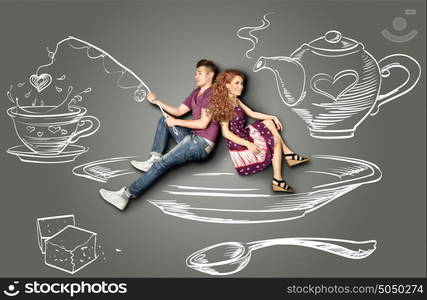 Happy valentines love story concept of a romantic couple sitting on a saucer and fishing in a teacup against chalk drawings background.