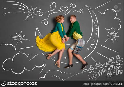 Happy valentines love story concept of a romantic couple sitting on the moon and holding hands against chalk drawings background of a night sky.