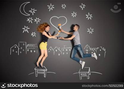 Happy valentines love story concept of a romantic couple standing on a stool and painting a heart in the night sky against chalk drawings background.