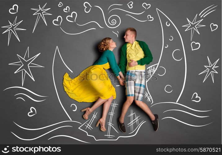 Happy valentines love story concept of a romantic couple swimming on the moon boat, holding hands and kissing against chalk drawings background of a night sky.