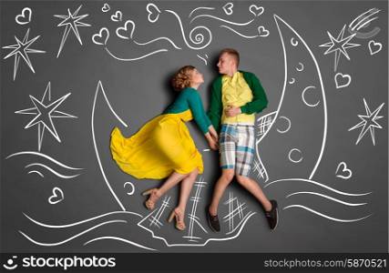 Happy valentines love story concept of a romantic couple swimming on the moon boat, holding hands and kissing against chalk drawings background of a night sky.