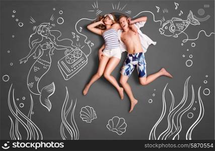 Happy valentines love story concept of a romantic couple swimming underwater, sharing headphones, and listening to the music against chalk drawings undersea background.