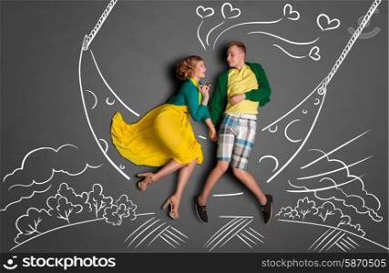 Happy valentines love story concept of a romantic couple swinging on the moon, holding hands and kissing against chalk drawings background of a night sky.