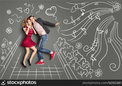 Happy valentines love story concept of a romantic couple walking in the park, sharing headphones and listening to the music against chalk drawings background.