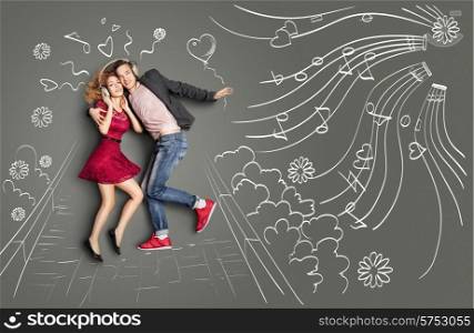 Happy valentines love story concept of a romantic couple walking in the park, sharing headphones and listening to the music against chalk drawings background.