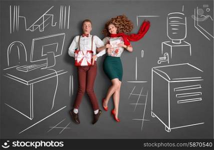 Happy valentines love story concept of an office romance. Young couple at work smiling at each other and sharing presents against chalk drawings background.