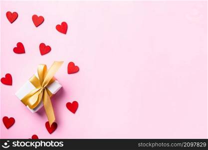 Happy Valentines&rsquo; day background concept. White gift box with a golden bow ribbon and wood red hearts composition for love isolated on pink background with copy space. Top View from above
