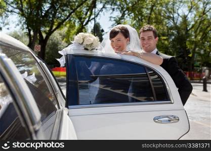 Happy wedding couple getting in car and looking at camera