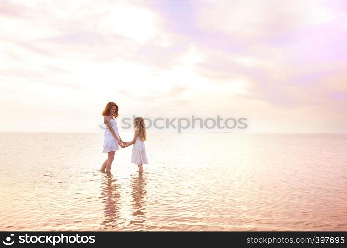 happy weekend by the sea - Mom and daughter in white dresses walking by the sea at sunset. Ukrainian landscape at the Sea of Azov, Ukraine
