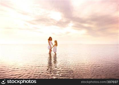 happy weekend by the sea - Mom and daughter in white dresses walking by the sea at sunset. Ukrainian landscape at the Sea of Azov, Ukraine