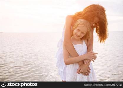 happy weekend by the sea - Mom and daughter in white dresses on the sea at sunset.