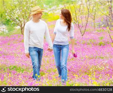 Happy wife and husband holding hands and looking each other walking on pink floral field, enjoying family, romantic relationship concept