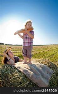 Happy woman and child eating bread in wheat field against blue sky background. Shot was taken with fisheye lens