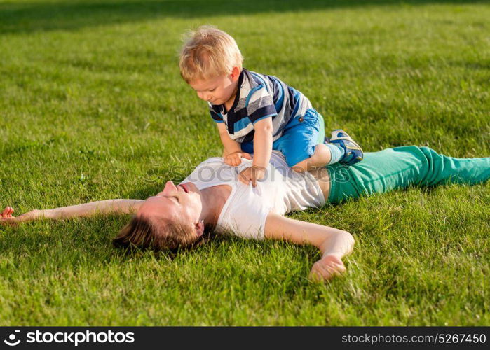 Happy woman and child having fun outdoor on meadow. Family lifestyle scene of mother and son resting together on green grass in the park.