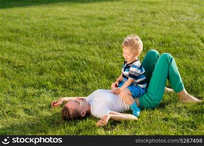 Happy woman and child having fun outdoor on meadow. Family lifestyle scene of mother and son resting together on green grass in the park.