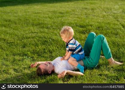 Happy woman and child having fun outdoor on meadow. Family lifestyle scene of mother and son resting together on green grass in the park.