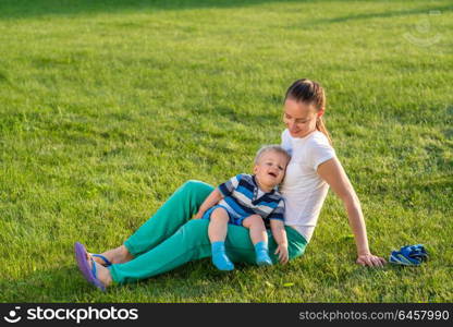 Happy woman and child having fun outdoor on meadow. Family lifestyle scene of mother and son resting together on green grass in the park.