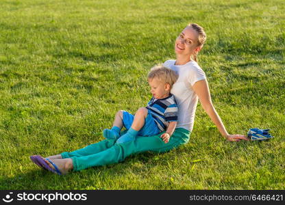 Happy woman and child having fun outdoor on meadow. Family lifestyle scene of mother and son resting together on green grass in the park.