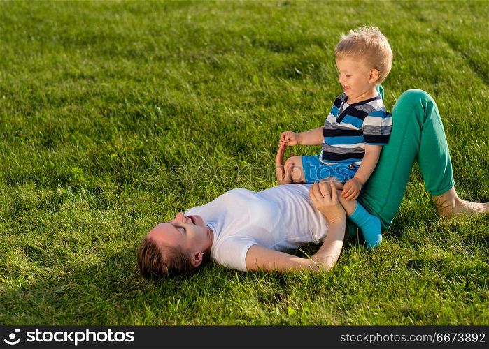 Happy woman and child having fun outdoor on meadow. Happy woman and child having fun outdoor on meadow. Family lifestyle scene of mother and son resting together on green grass in the park.