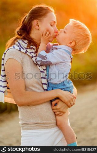 Happy woman and child having fun outdoors. Family lifestyle rural scene of mother and son in sunset sunlight. Mother kissing her son.