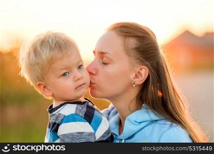 Happy woman and child having fun outdoors. Family lifestyle rural scene of mother and son in sunset sunlight. Mother kissing her son.
