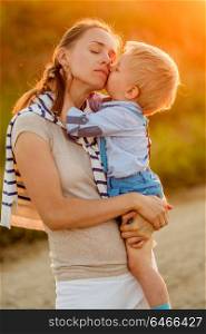 Happy woman and child having fun outdoors. Family lifestyle rural scene of mother and son in sunset sunlight. Boy kissing his mom.