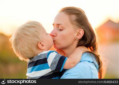 Happy woman and child having fun outdoors. Family lifestyle rural scene of mother and son in sunset sunlight. Boy kissing his mom.