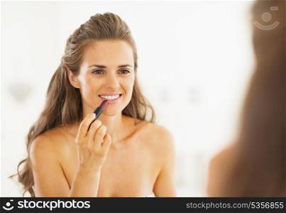 Happy woman applying lipstick in bathroom