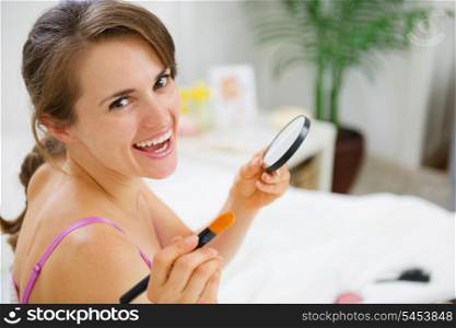 Happy woman applying make up in bedroom