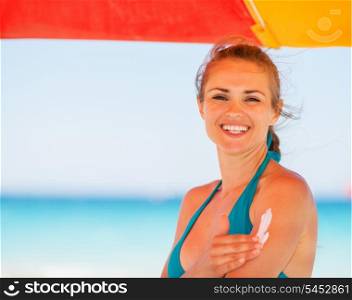 Happy woman applying sun block creme on arm