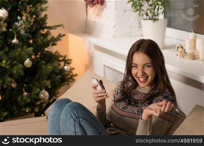 Happy woman at home reading a text message while sitting on sofa