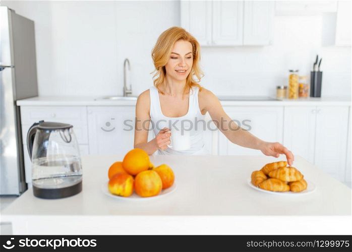 Happy woman at the table, fruit breakfast on the kitchen. Female person at home in the morning, healthy nutrition and lifestyle