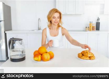 Happy woman at the table, fruit breakfast on the kitchen. Female person at home in the morning, healthy nutrition and lifestyle