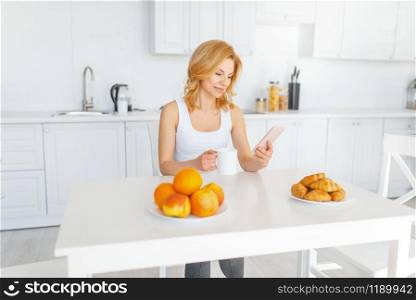 Happy woman at the table with fruits and baking, breakfast on the kitchen. Female person at home in the morning, healthy nutrition and lifestyle