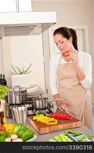 Happy woman biting red pepper in modern kitchen, cooking
