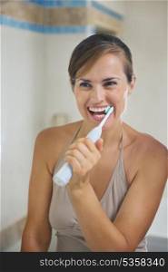 Happy woman brushing teeth with electric toothbrush