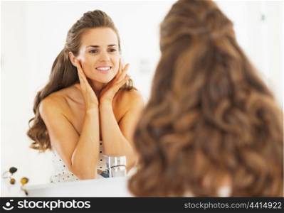 Happy woman checking facial skin condition in bathroom