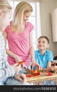 Happy woman chopping red bell pepper while standing with children in kitchen