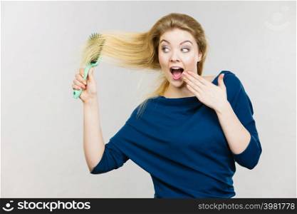 Happy woman combing her hair with brush. Young smiling female with natural blond straight long hairs, studio shot on grey. Woman brushing her long hair with brush