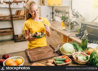 Happy woman cooking salad on the kitchen, healthy bio food preparing. Vegetarian diet, fresh vegetables and fruits on wooden table