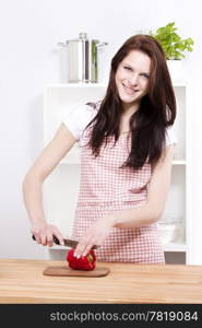 happy woman cutting paprika for salad. happy young woman in kitchen cutting red paprika for salad