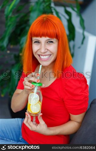 Happy woman drinking a lemonade in a glass jar with a straw at home