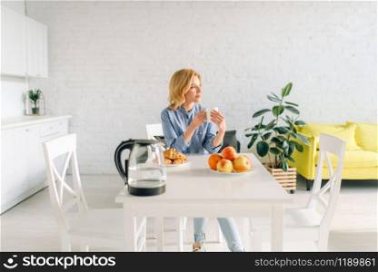 Happy woman drinks coffee with milk, breakfast on the kitchen. Female person at home in the morning, healthy nutrition and lifestyle
