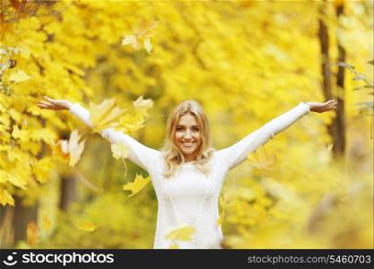 Happy woman drop up leaves in autumn park