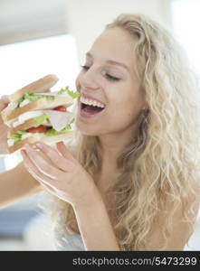 Happy woman eating large sandwich in house