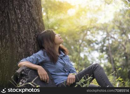 Happy woman enjoy and relax with the nature. Young beautiful woman sitting under the big tree in green forest.