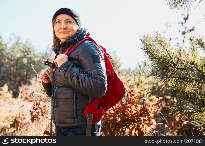 Happy woman enjoying hike on sunny vacation day. Female with backpack walking through forest. Spending summer vacation close to nature