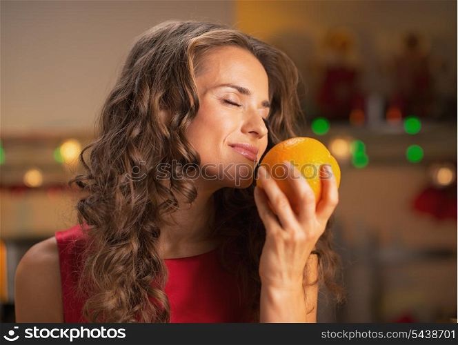 Happy woman enjoying orange in christmas decorated kitchen