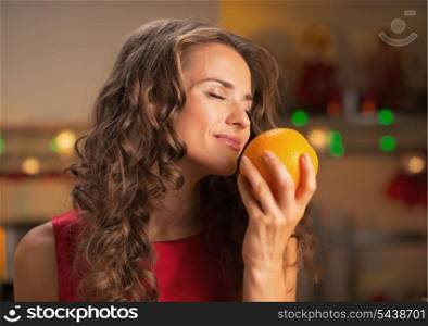 Happy woman enjoying orange in christmas decorated kitchen