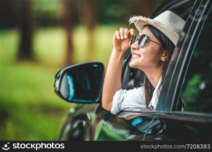 Happy woman hand holding hat outside open window car with green forest woods mountain background. People lifestyle relaxing as traveler on road trip in holiday vacation. Transportation and travel